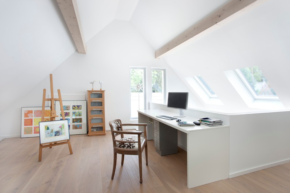 This is an example of an expansive scandinavian study room in Berlin with white walls, light hardwood floors, no fireplace and a freestanding desk.