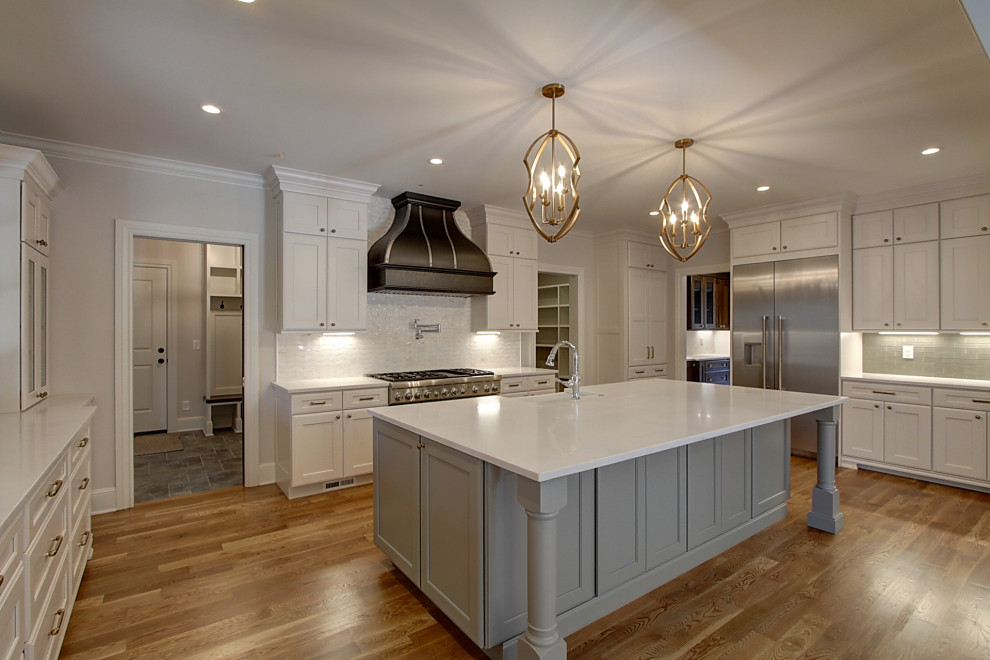 Expansive transitional u-shaped eat-in kitchen in Denver with a farmhouse sink, shaker cabinets, white cabinets, quartz benchtops, white splashback, subway tile splashback, stainless steel appliances, medium hardwood floors, with island, brown floor and white benchtop.