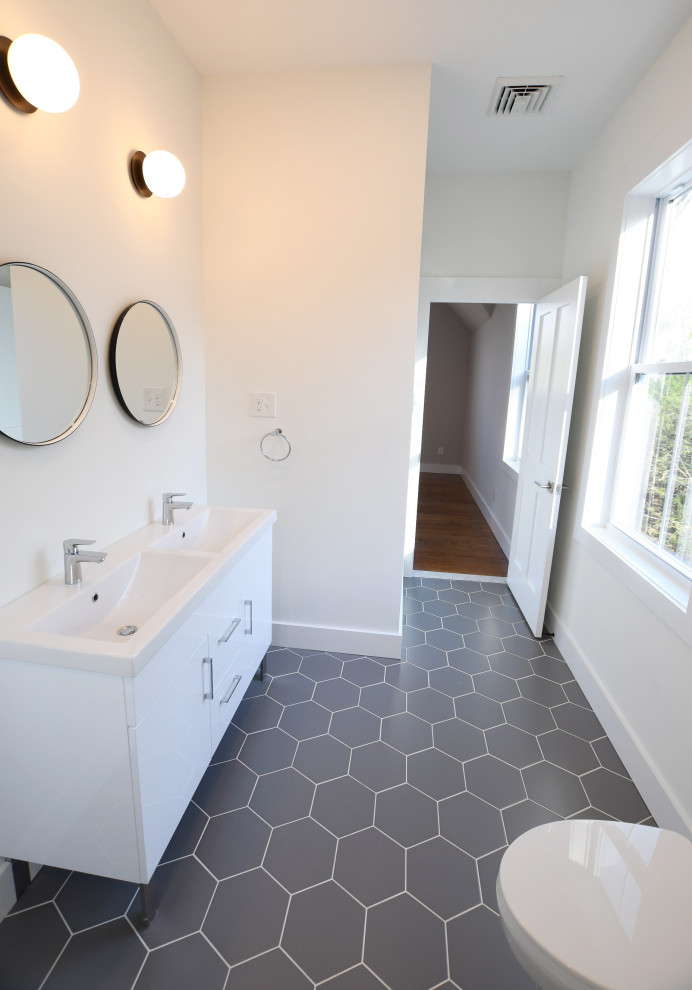 Photo of a mid-sized country master bathroom in New York with flat-panel cabinets, white cabinets, an alcove shower, a one-piece toilet, white tile, ceramic tile, white walls, ceramic floors, an integrated sink, solid surface benchtops, grey floor, white benchtops, a double vanity, a freestanding vanity and vaulted.