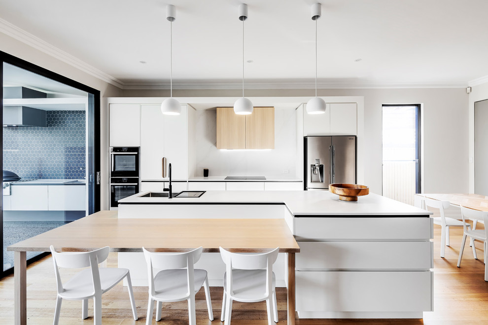 Inspiration for a contemporary galley eat-in kitchen in Adelaide with an undermount sink, flat-panel cabinets, white cabinets, white splashback, stainless steel appliances, medium hardwood floors, with island, brown floor and white benchtop.