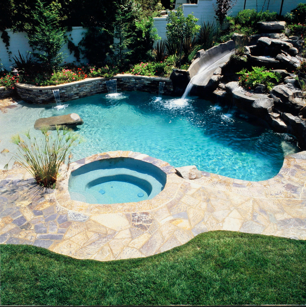 This is an example of a tropical backyard pool in Orange County with a water feature and stamped concrete.