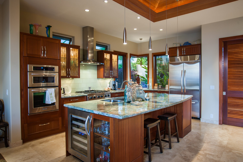 Design ideas for a mid-sized tropical l-shaped open plan kitchen in Hawaii with with island, granite benchtops, stainless steel appliances, a double-bowl sink, glass-front cabinets, medium wood cabinets, white splashback, porcelain splashback, ceramic floors and beige floor.