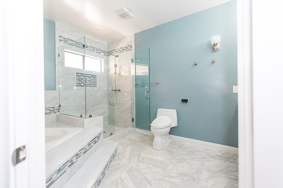This is an example of a mid-sized modern master bathroom in Other with shaker cabinets, blue cabinets, a drop-in tub, a corner shower, a one-piece toilet, white tile, marble, blue walls, marble floors, an undermount sink, quartzite benchtops, white floor, a hinged shower door and white benchtops.
