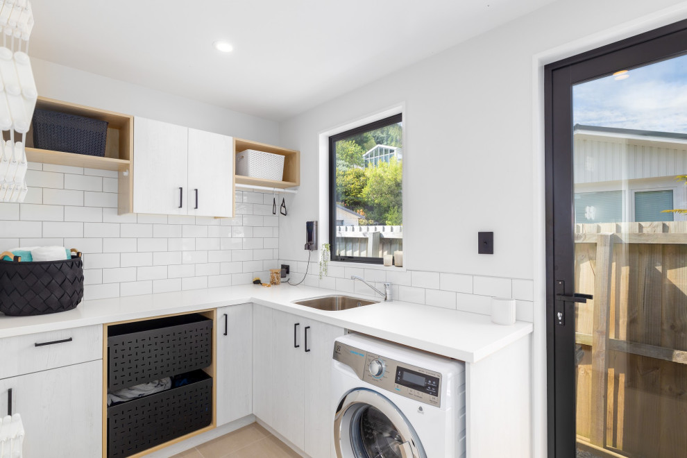 Large contemporary galley utility room in Christchurch with a submerged sink, white cabinets, engineered stone countertops, grey splashback, metro tiled splashback, laminate floors, white worktops, a vaulted ceiling and white walls.