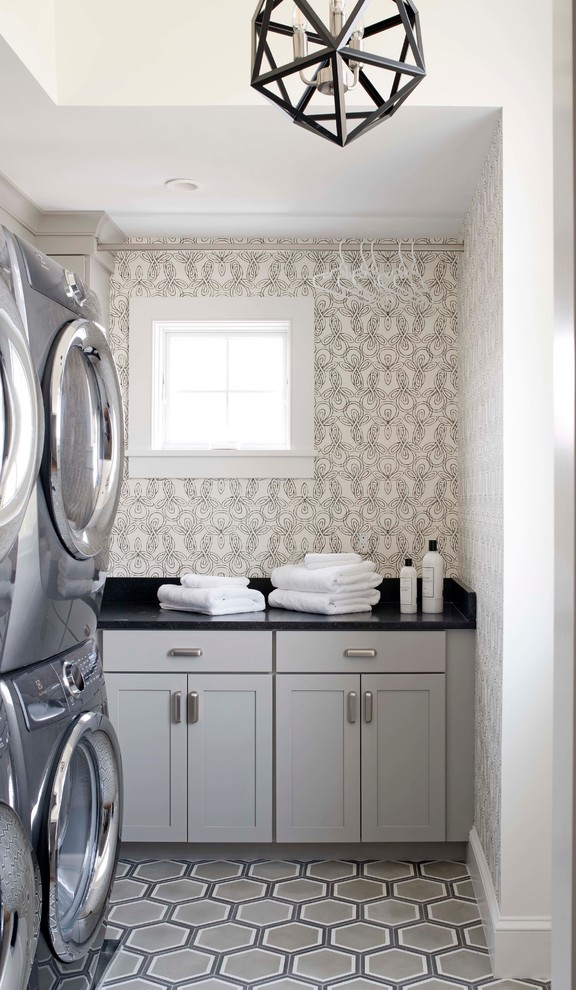 This is an example of a beach style dedicated laundry room in Portland Maine with shaker cabinets, grey cabinets, multi-coloured walls, a stacked washer and dryer, multi-coloured floor and black benchtop.