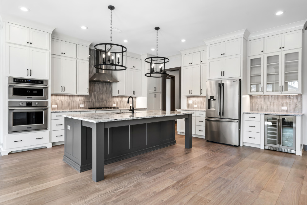 Mid-sized transitional l-shaped medium tone wood floor and brown floor open concept kitchen photo with recessed-panel cabinets, white cabinets, quartz countertops, beige backsplash, ceramic backsplash, stainless steel appliances and an island