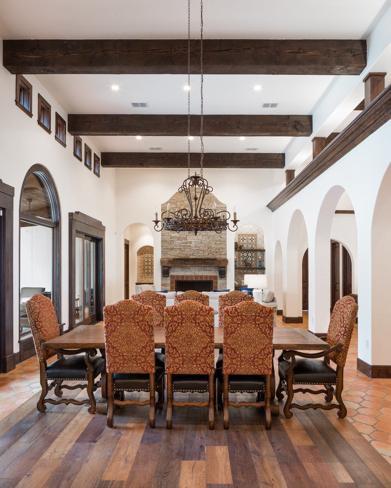 This is an example of a large mediterranean open plan dining in Austin with white walls, medium hardwood floors, a standard fireplace, a tile fireplace surround and brown floor.