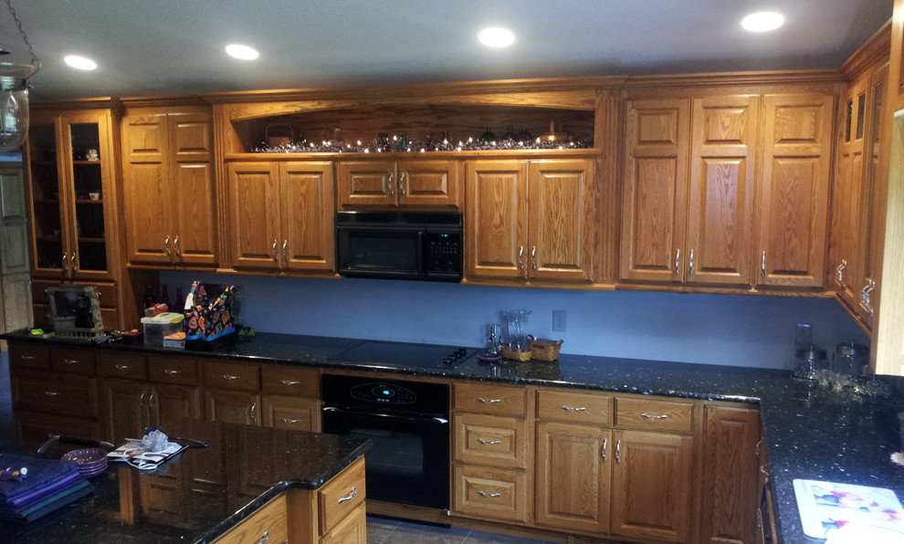 Photo of a mid-sized traditional kitchen in Chicago with raised-panel cabinets, medium wood cabinets, granite benchtops, black appliances, with island, porcelain floors and grey floor.
