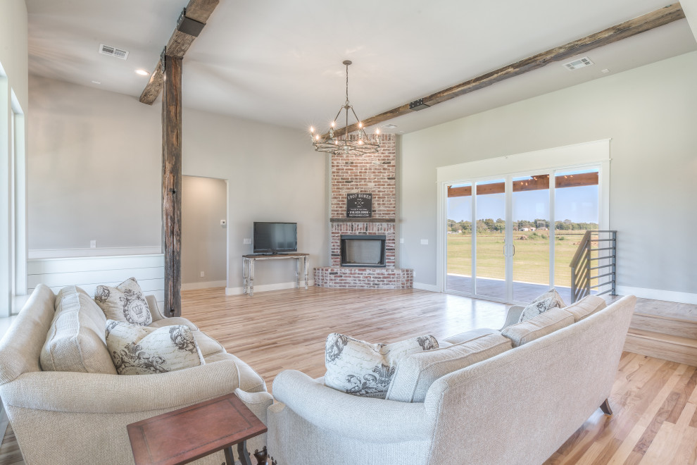 Photo of a mid-sized country formal open concept living room in Other with grey walls, medium hardwood floors, a corner fireplace, a brick fireplace surround, a freestanding tv and brown floor.