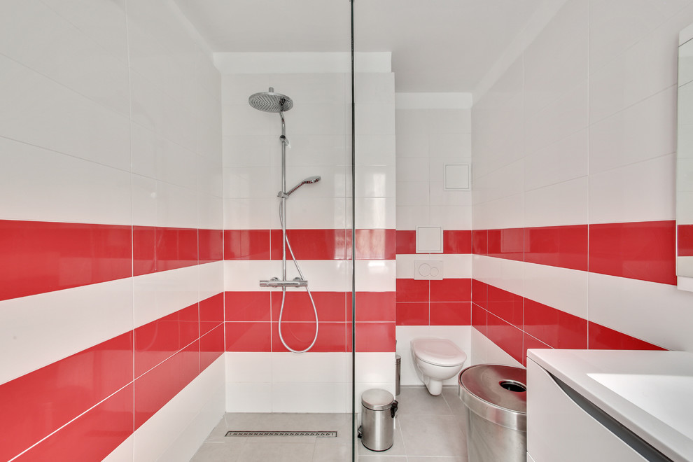 This is an example of a contemporary 3/4 bathroom in Paris with flat-panel cabinets, white cabinets, a curbless shower, a wall-mount toilet, an integrated sink, an open shower, white benchtops, red tile, white tile, white walls and grey floor.