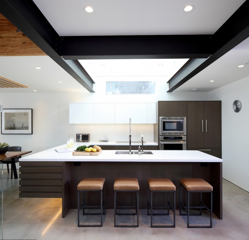 This is an example of a contemporary u-shaped open plan kitchen in Vancouver with flat-panel cabinets, dark wood cabinets, concrete floors and a peninsula.