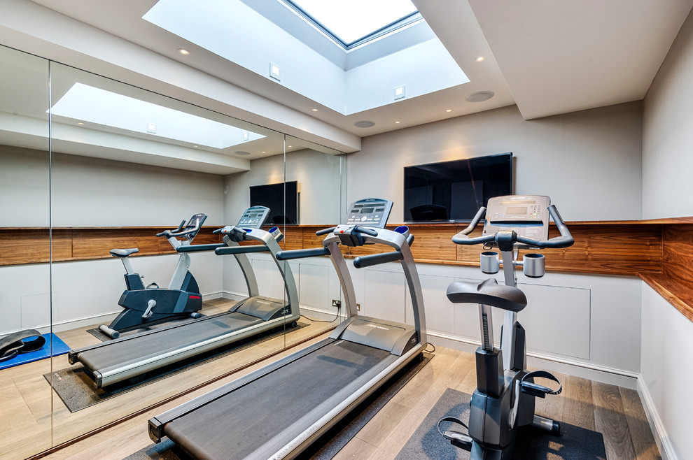 Photo of a small contemporary multipurpose gym in London with white walls and light hardwood floors.