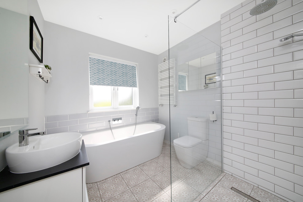 Mid-sized contemporary kids bathroom in London with flat-panel cabinets, white cabinets, a freestanding tub, an open shower, a two-piece toilet, white tile, subway tile, grey walls, porcelain floors, a vessel sink, engineered quartz benchtops, multi-coloured floor, an open shower and black benchtops.
