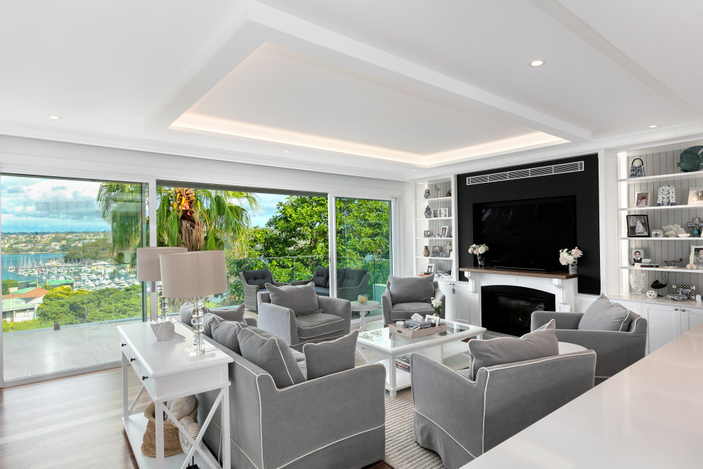 Inspiration for a large beach style open concept living room in Sydney with white walls, medium hardwood floors, a standard fireplace, a stone fireplace surround, a built-in media wall, recessed and decorative wall panelling.