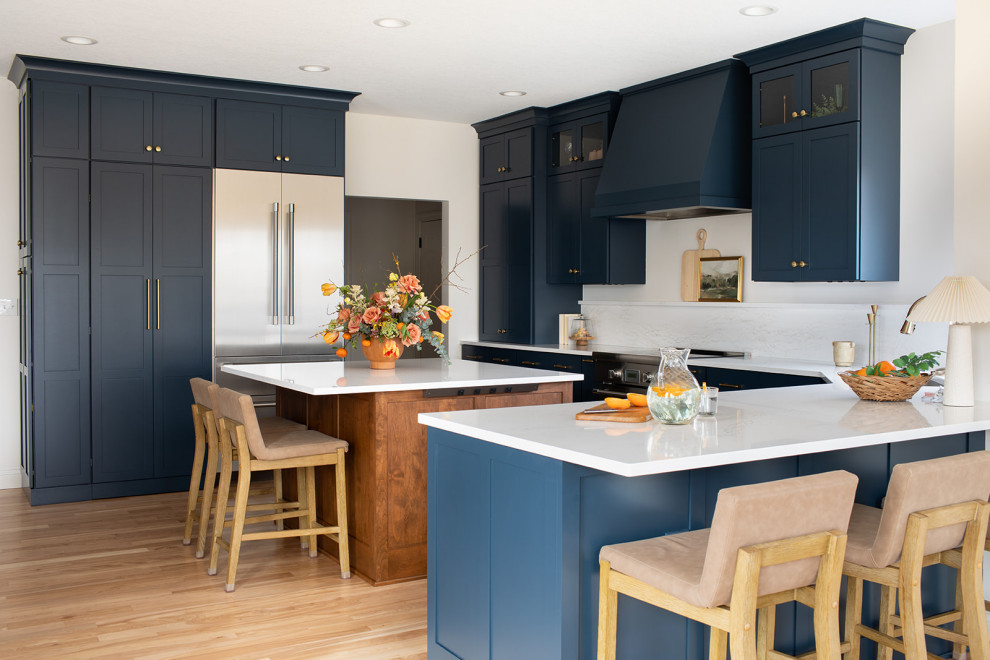 Example of a large transitional light wood floor kitchen design with an undermount sink, shaker cabinets, blue cabinets, quartz countertops, white backsplash, quartz backsplash, stainless steel appliances, an island and white countertops