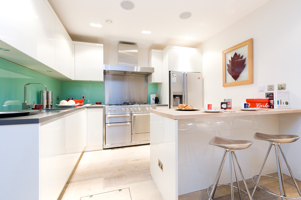 Inspiration for a mid-sized contemporary l-shaped eat-in kitchen in London with an undermount sink, flat-panel cabinets, white cabinets, glass sheet splashback, stainless steel appliances, light hardwood floors and a peninsula.