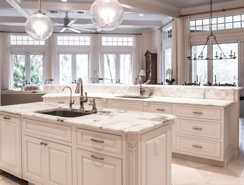 Large transitional u-shaped limestone floor and white floor open concept kitchen photo in Orlando with an undermount sink, raised-panel cabinets, white cabinets, marble countertops, gray backsplash, marble backsplash, stainless steel appliances and two islands