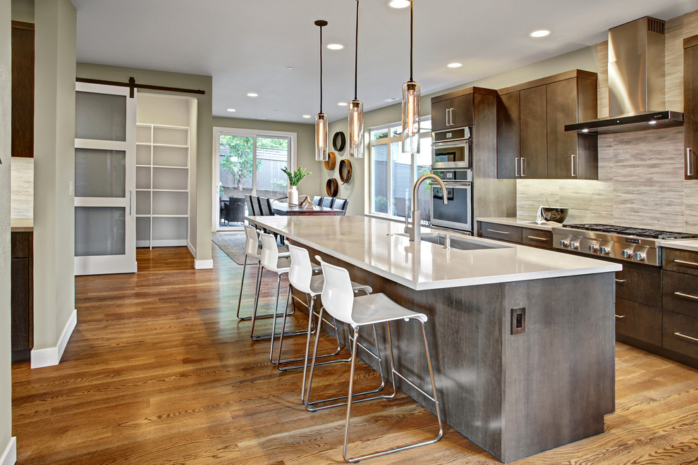 This is an example of a contemporary l-shaped eat-in kitchen in Seattle with flat-panel cabinets, dark wood cabinets, stainless steel appliances, medium hardwood floors, with island, an undermount sink, quartz benchtops, grey splashback and stone tile splashback.