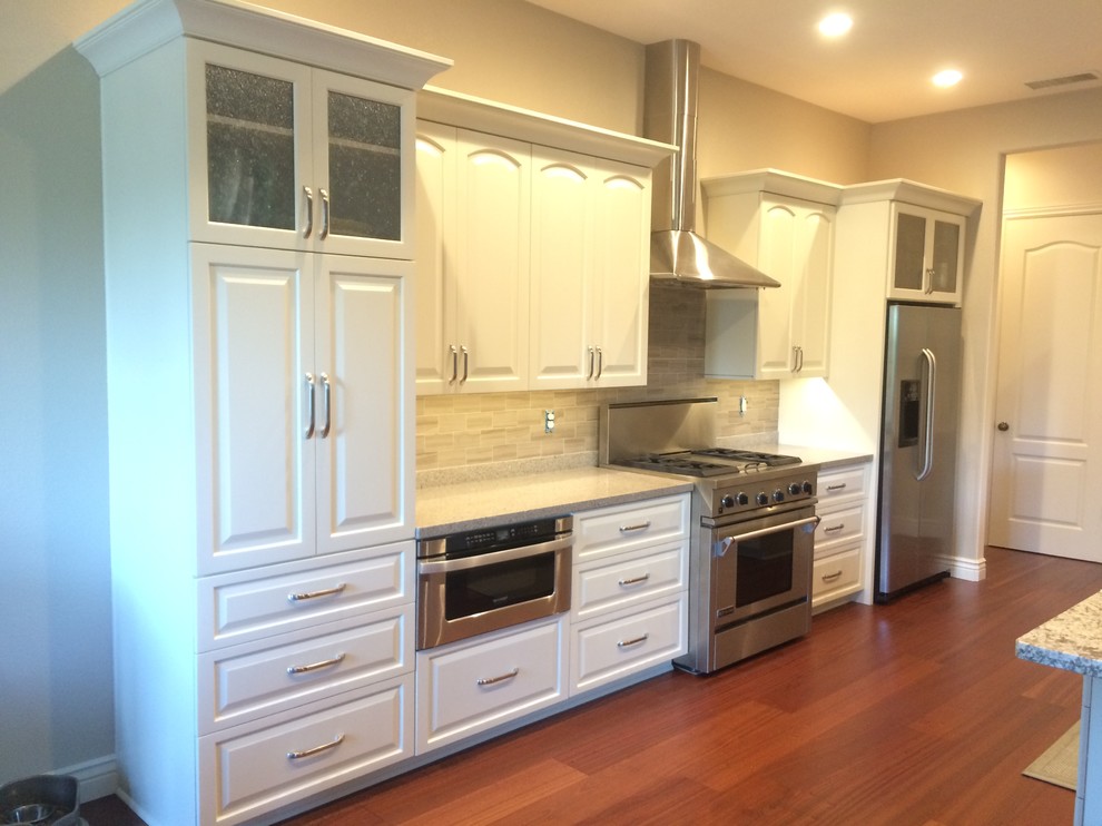 This is an example of a large traditional u-shaped eat-in kitchen in Sacramento with an undermount sink, raised-panel cabinets, white cabinets, granite benchtops, grey splashback, porcelain splashback, stainless steel appliances, medium hardwood floors, with island and brown floor.