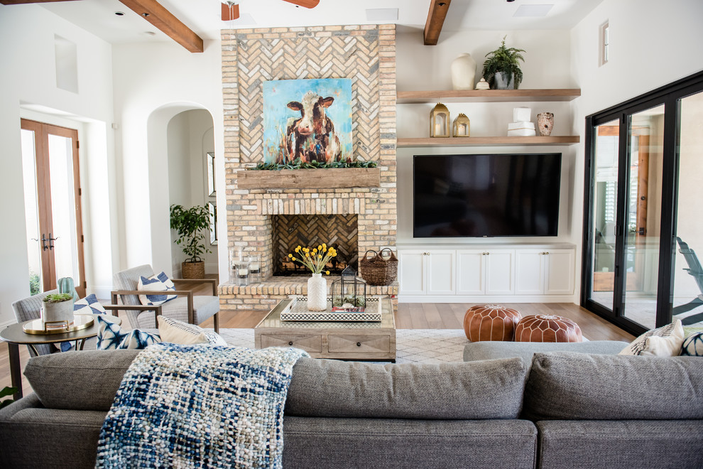 This is an example of an expansive eclectic open concept family room in Phoenix with white walls, medium hardwood floors, a standard fireplace, a brick fireplace surround and a wall-mounted tv.