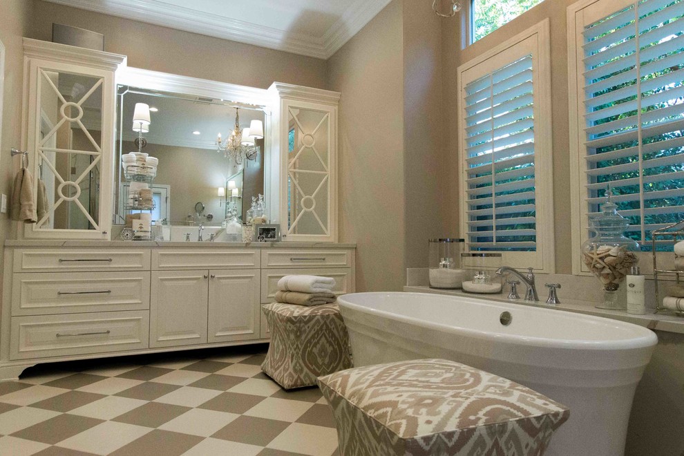 Example of a large classic master multicolored floor freestanding bathtub design with raised-panel cabinets, white cabinets, a one-piece toilet, beige walls, an undermount sink, a hinged shower door, marble countertops and white countertops