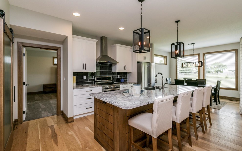 Inspiration for a transitional galley medium tone wood floor and brown floor eat-in kitchen remodel with a farmhouse sink, shaker cabinets, white cabinets, black backsplash, subway tile backsplash, stainless steel appliances, an island and gray countertops