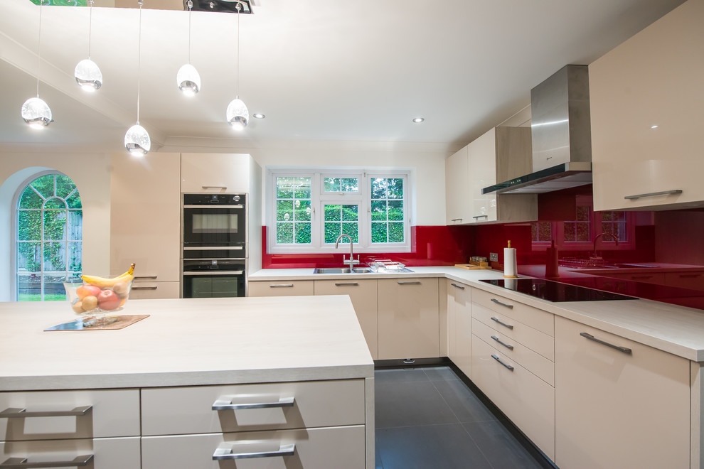 This is an example of a contemporary l-shaped kitchen in London with a double-bowl sink, flat-panel cabinets, light wood cabinets, onyx benchtops, red splashback, glass sheet splashback, black appliances and with island.