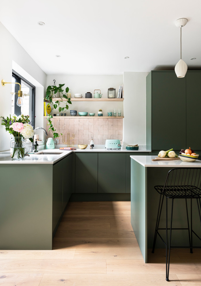 Large contemporary l-shaped open plan kitchen in London with a single-bowl sink, green cabinets, white splashback, coloured appliances, light hardwood floors, with island, brown floor and white benchtop.