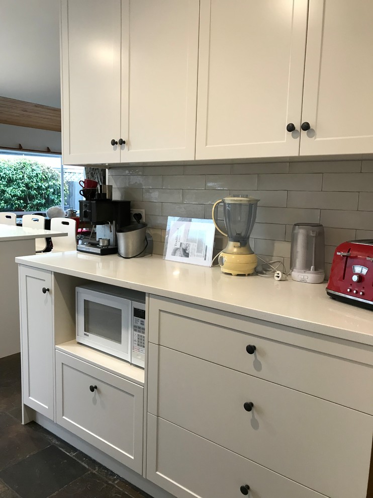 Design ideas for a large contemporary u-shaped open plan kitchen in Christchurch with a single-bowl sink, recessed-panel cabinets, white cabinets, quartz benchtops, grey splashback, subway tile splashback, stainless steel appliances, slate floors, a peninsula, black floor and white benchtop.