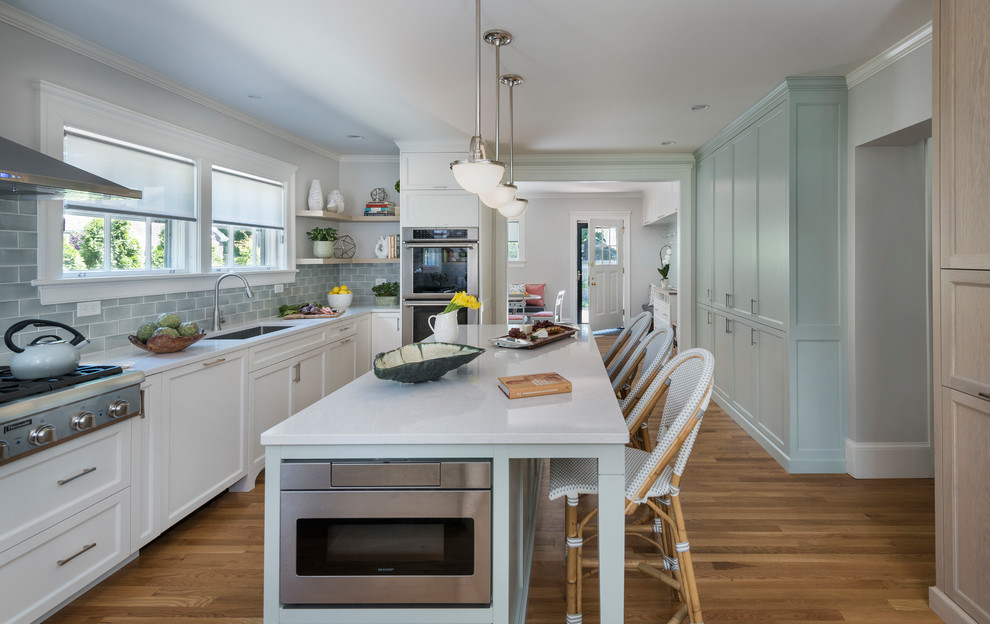 Photo of a beach style kitchen in Providence with an undermount sink, shaker cabinets, white cabinets, blue splashback, subway tile splashback, stainless steel appliances, medium hardwood floors, with island and white benchtop.