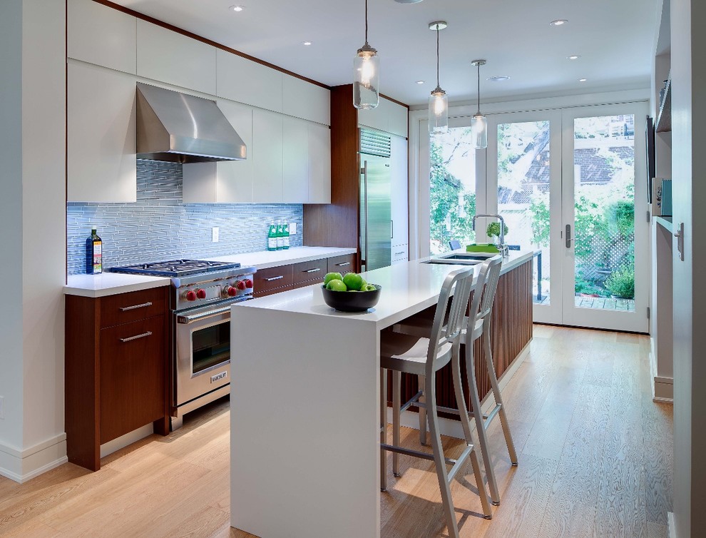 Mid-sized midcentury galley eat-in kitchen in Toronto with an undermount sink, flat-panel cabinets, medium wood cabinets, quartz benchtops, blue splashback, glass tile splashback, stainless steel appliances, light hardwood floors and with island.