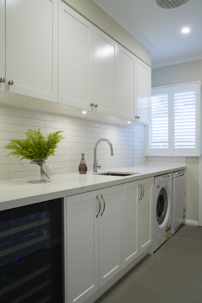 This is an example of a mid-sized traditional galley utility room in Melbourne with an undermount sink, shaker cabinets, white cabinets, quartz benchtops, porcelain floors and a side-by-side washer and dryer.