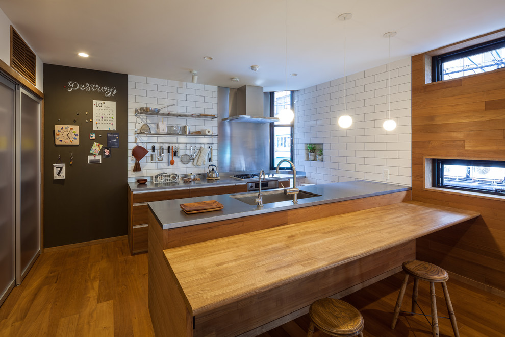 Photo of an asian galley open plan kitchen in Berlin with an undermount sink, flat-panel cabinets, medium wood cabinets, stainless steel benchtops, white splashback, stainless steel appliances, medium hardwood floors and a peninsula.