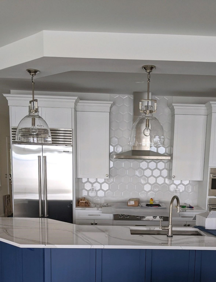 Example of a mid-sized transitional kitchen design with an undermount sink, recessed-panel cabinets, white cabinets, quartz countertops, white backsplash, ceramic backsplash, stainless steel appliances, an island and white countertops