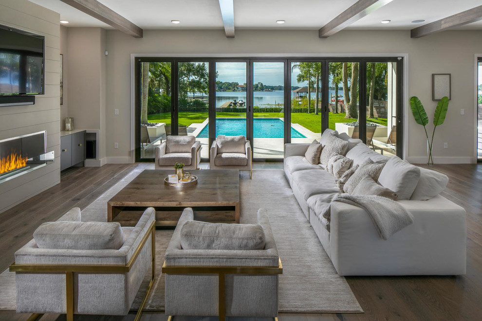 This is an example of an expansive modern open concept living room in Tampa with white walls, medium hardwood floors, a wood fireplace surround, a wall-mounted tv and brown floor.