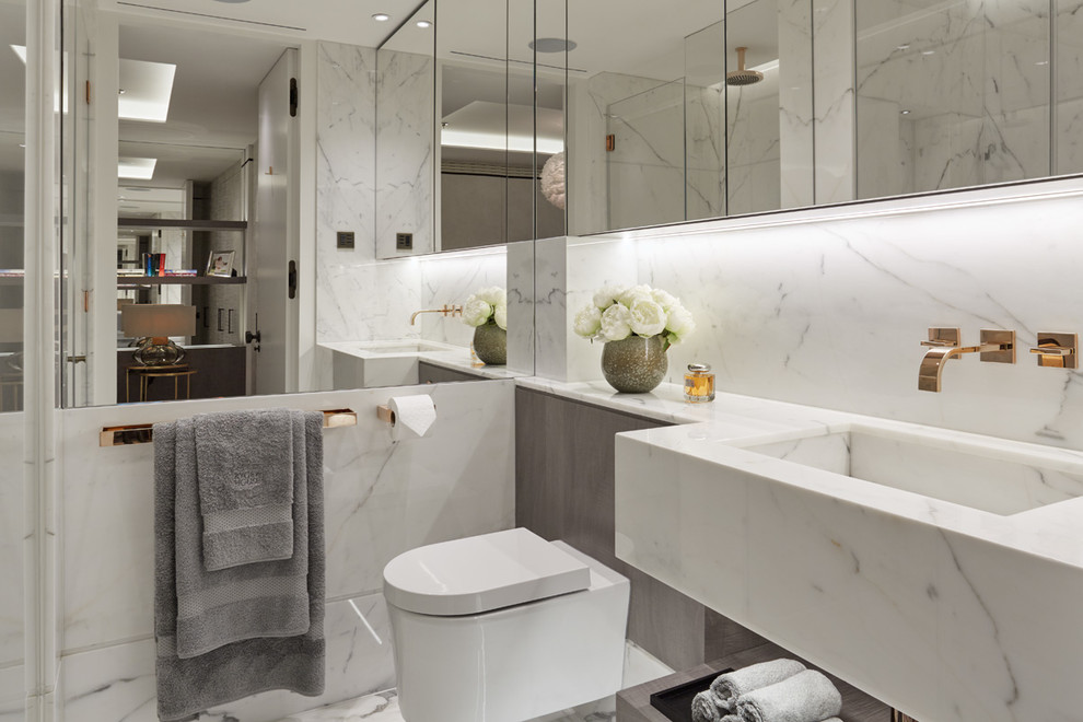 This is an example of a contemporary bathroom in London with a wall-mount toilet, an integrated sink, marble benchtops and marble.