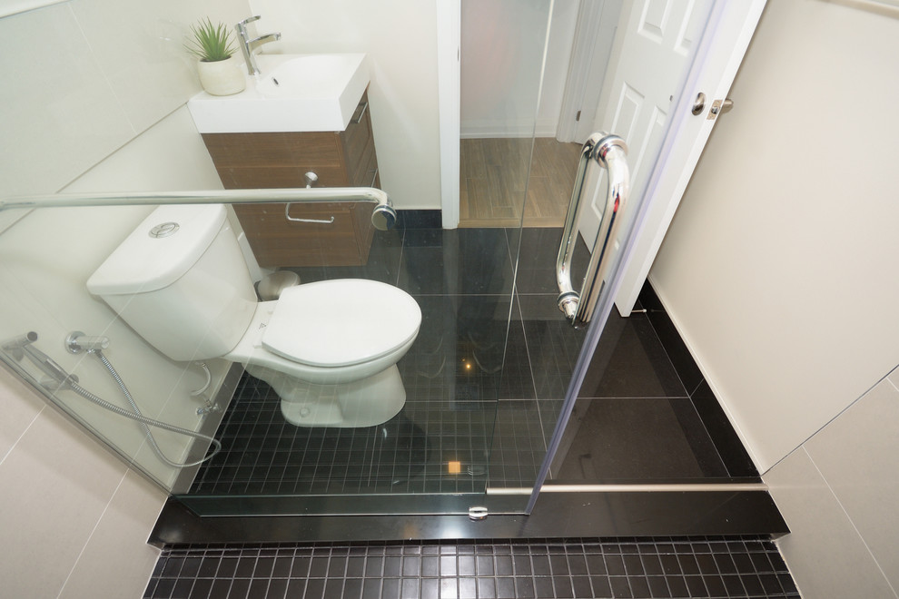 Mid-sized transitional 3/4 bathroom in Toronto with shaker cabinets, brown cabinets, a double shower, a two-piece toilet, black tile, ceramic tile, white walls, porcelain floors and a wall-mount sink.