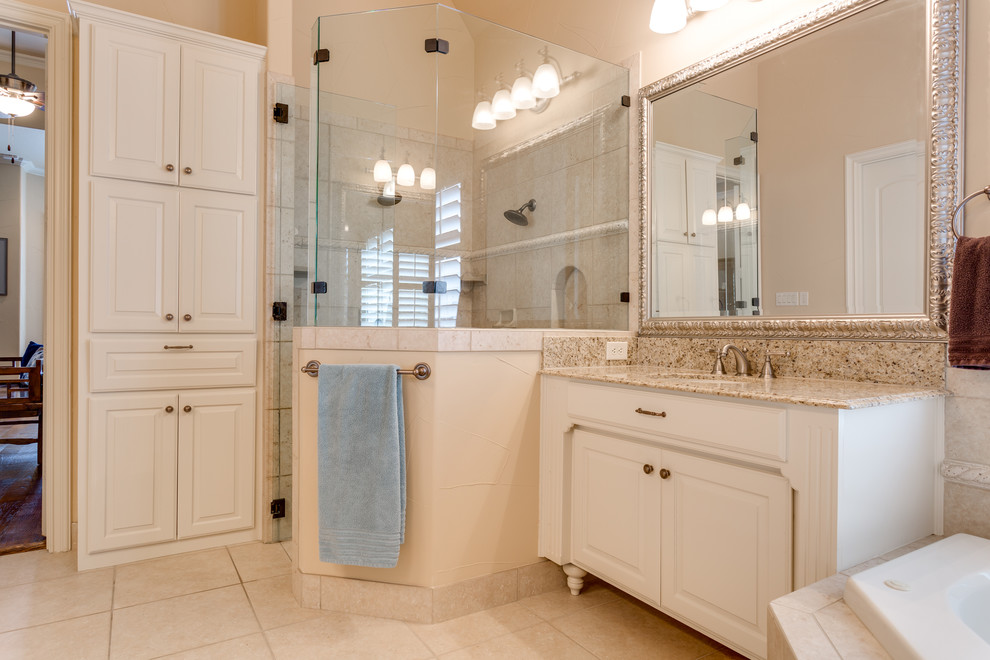 This is an example of a large transitional master bathroom in Dallas with raised-panel cabinets, white cabinets, a corner tub, a corner shower, a two-piece toilet, black tile, ceramic tile, beige walls, ceramic floors, an undermount sink and granite benchtops.
