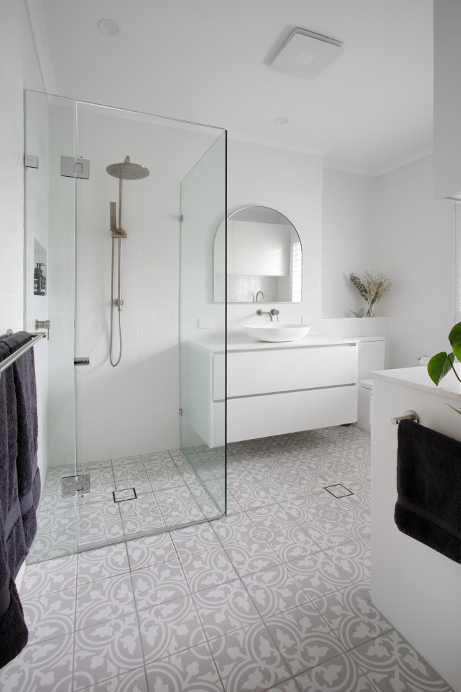 This is an example of a mid-sized transitional bathroom in Brisbane with flat-panel cabinets, white cabinets, a corner shower, a one-piece toilet, white tile, cement tile, white walls, ceramic floors, a vessel sink, engineered quartz benchtops, grey floor, a hinged shower door, white benchtops, a laundry, a single vanity and a floating vanity.