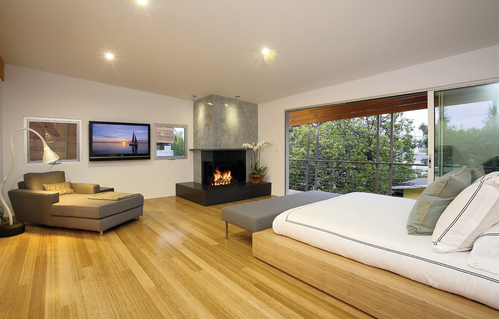 Large modern master bedroom in Los Angeles with white walls, light hardwood floors, a standard fireplace and a concrete fireplace surround.