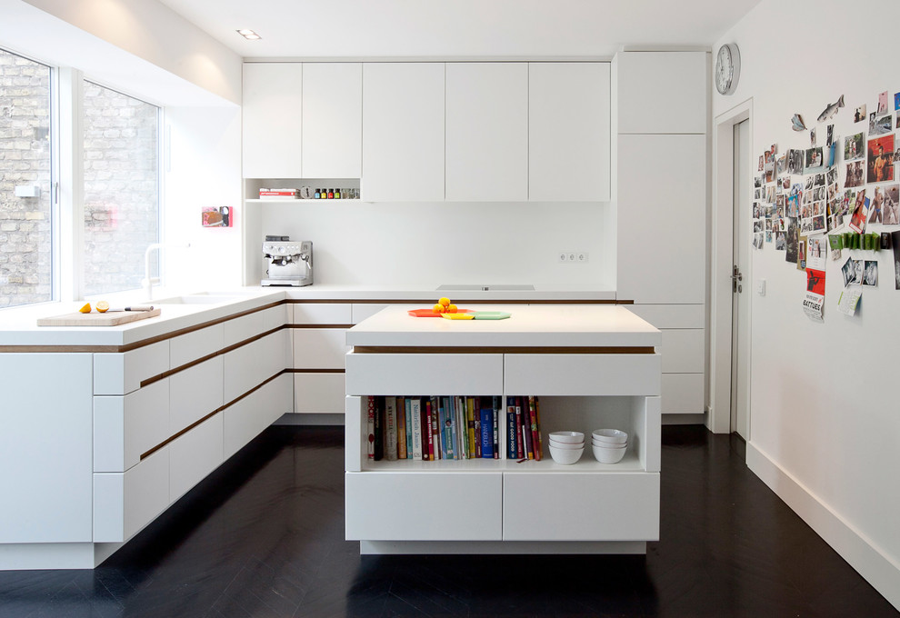 Photo of a mid-sized contemporary l-shaped open plan kitchen in Frankfurt with an integrated sink, flat-panel cabinets, white cabinets, solid surface benchtops, white splashback, white appliances, dark hardwood floors and with island.