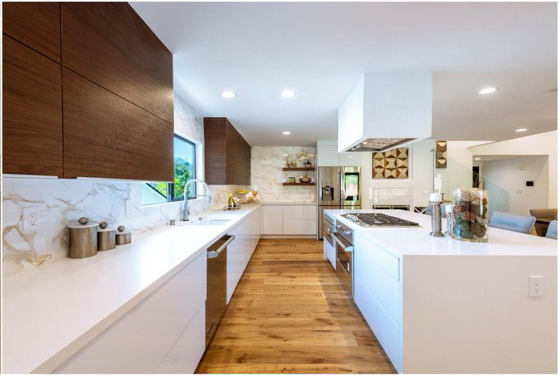 Transitional galley eat-in kitchen in Orange County with a drop-in sink, flat-panel cabinets, white cabinets, solid surface benchtops, multi-coloured splashback, marble splashback, stainless steel appliances, light hardwood floors, multiple islands, brown floor, white benchtop and exposed beam.