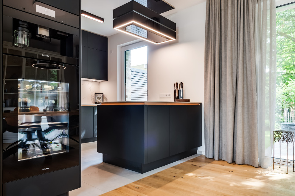 Mid-sized modern l-shaped separate kitchen in Hamburg with a single-bowl sink, flat-panel cabinets, black cabinets, quartzite benchtops, beige splashback, ceramic splashback, black appliances, ceramic floors, a peninsula, beige floor, beige benchtop and recessed.