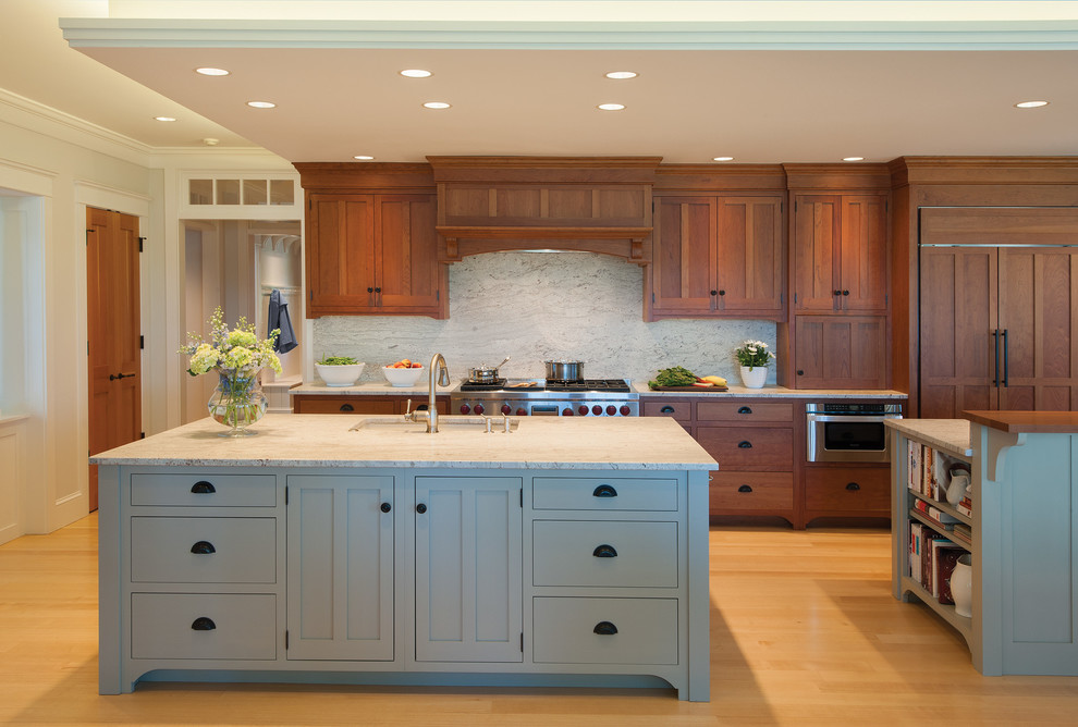This is an example of a large arts and crafts single-wall eat-in kitchen in Portland Maine with medium wood cabinets, granite benchtops, stone slab splashback, light hardwood floors, multiple islands, a single-bowl sink, shaker cabinets, white splashback and stainless steel appliances.