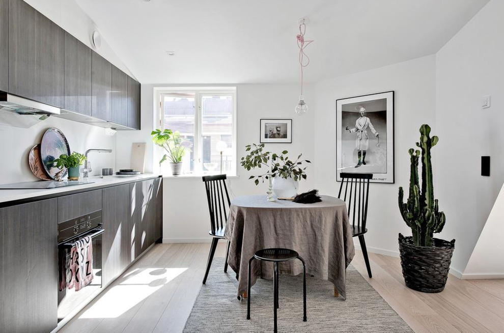 Mid-sized scandinavian single-wall eat-in kitchen in Gothenburg with flat-panel cabinets, dark wood cabinets, white splashback, black appliances, light hardwood floors, marble benchtops and no island.