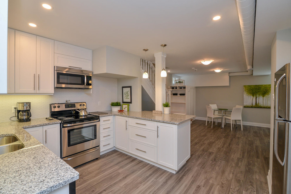 Example of a mid-sized transitional u-shaped medium tone wood floor and gray floor open concept kitchen design with an undermount sink, shaker cabinets, white cabinets, granite countertops, stainless steel appliances and a peninsula
