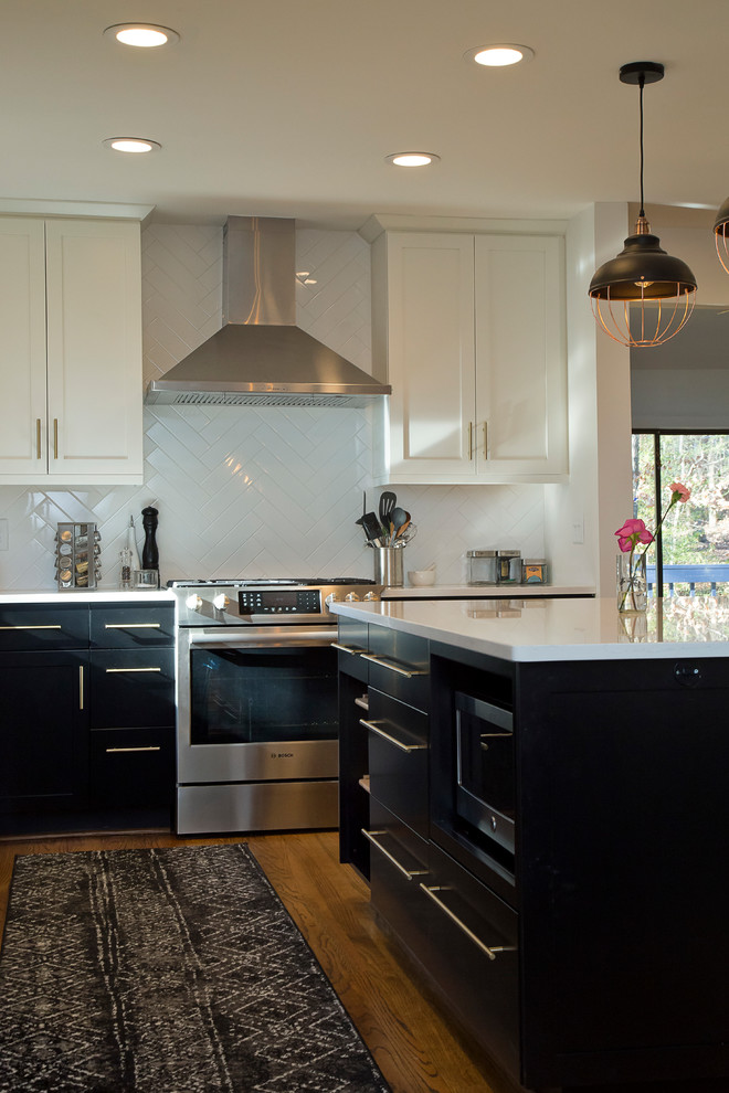 This is an example of a mid-sized industrial l-shaped eat-in kitchen in Raleigh with an undermount sink, shaker cabinets, black cabinets, quartz benchtops, white splashback, ceramic splashback, stainless steel appliances, medium hardwood floors, with island, brown floor and white benchtop.