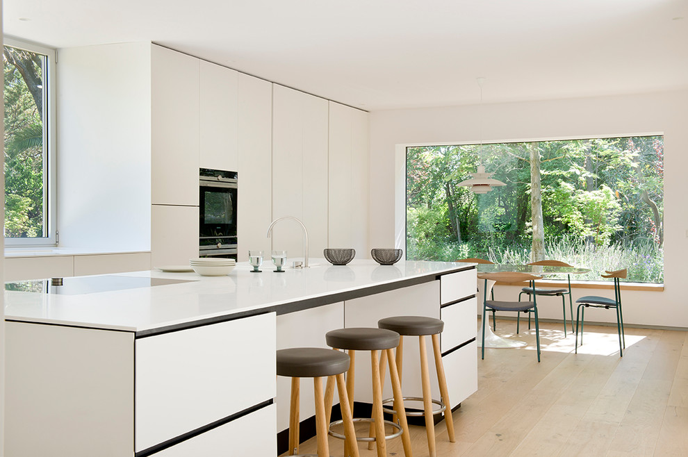 Large contemporary single-wall kitchen in Madrid with flat-panel cabinets, white cabinets, quartz benchtops, medium hardwood floors, with island and beige floor.