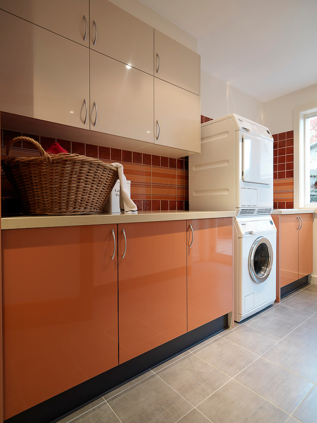 Photo of a large modern galley dedicated laundry room in Melbourne with an undermount sink, flat-panel cabinets, quartz benchtops, white walls, porcelain floors, a stacked washer and dryer and orange cabinets.