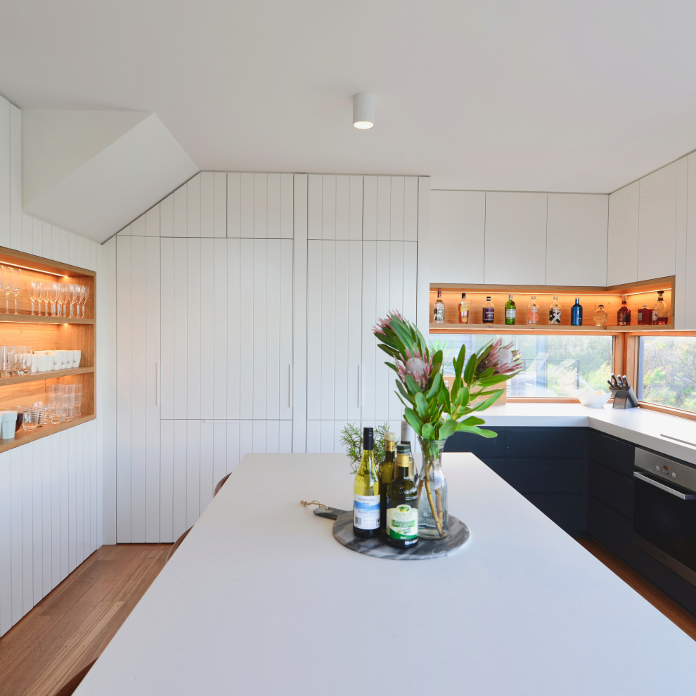 Design ideas for a mid-sized beach style l-shaped eat-in kitchen in Melbourne with a double-bowl sink, white cabinets, quartz benchtops, window splashback, stainless steel appliances, medium hardwood floors, with island, brown floor and grey benchtop.